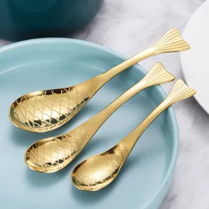 Kreative goldene Edelstahllöffel in Fischform für Dessert und Kaffee auf einem blauen Teller.
