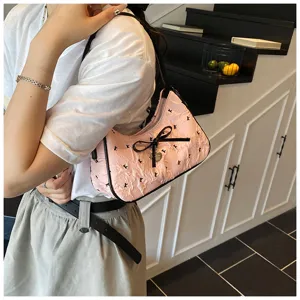 Macro detail of a pink crescent shoulder bag featuring a black bow and heart charm