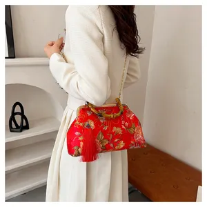 Détail du sac brodé rouge avec poignée en bambou et grand pompon de soirée chic.