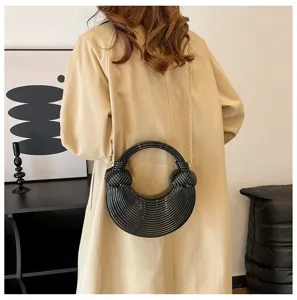 Black acrylic striped shell bag with gold chain strap carried over a beige trench coat.