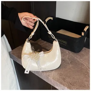 Detail einer cremeweißen Hobo-Tasche mit Herz-Perlen-Anhänger und Schleifendekor.