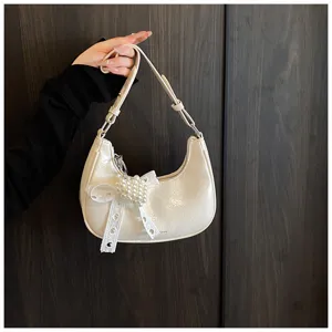 Detail einer cremefarbenen Hobo-Tasche aus Ölwachsleder mit Spitzenbogen und Perlenherz