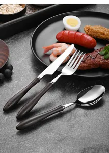 Detail of vintage wooden handle cutlery set on a black dinner plate with food