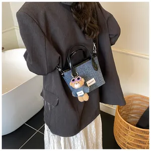Fashionable blue denim bucket bag with black handles and a cute bear charm accessory