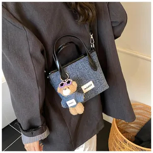 Detail of blue denim bucket bag with teddy bear charm worn with a stylish grey blazer