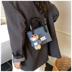 Detail view showing a denim blue bucket bag with a cute teddy bear charm on a blazer.