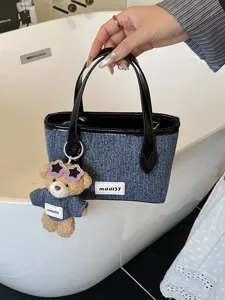Denim blue minimalist bucket bag with a cute bear charm, hand-held by a white bathtub.