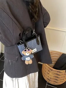 Stylish denim blue bucket handbag with black handles and bear charm worn by a model