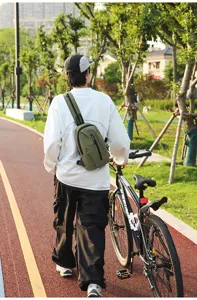 Detailed view of an olive green outdoor nylon chest bag worn while walking a bicycle in a park