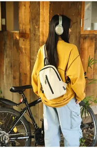Back view of a person wearing a cream nylon sling bag while cycling outdoors
