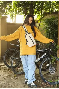 Model wearing a beige outdoor nylon sling bag while standing with a bicycle outdoors