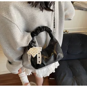 Vue détaillée d'un sac à main noir plissé avec un charme de nœud en perle blanche