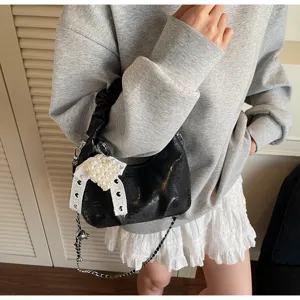 Détail du sac à main plissé noir avec un nœud en perles en forme de cœur et chaîne.
