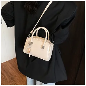 Close-up detail of a cream-colored pillow handbag with a pearl charm and black blazer