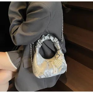 Détail du sac à main argenté plissé orné d'un pendentif cœur perlé et d'un nœud.