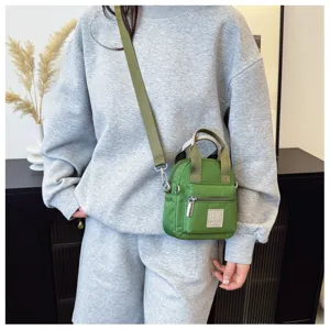 Detailansicht einer grünen Mini-Umhängetasche aus Nylon, getragen zu einem grauen Outfit.