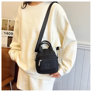 Detail einer schwarzen Nylon-Mini-Umhängetasche mit lässigem cremefarbenem Sweatshirt