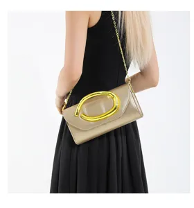 Modell trägt eine goldene Abend-Clutch mit klobigem Metallring und Kettenriemen