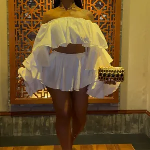 Detail view of white off-shoulder ruffled crop top and mini skirt set in indoor setting.