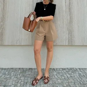 Detail view of casual high-waist pleated shorts with chic summer outfit and accessories.