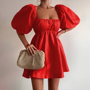 Close-up detail of red square neck puff sleeve mini dress with woven straw clutch bag.