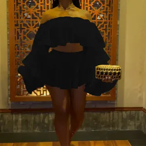 Detail view of the stylish black off-shoulder ruffled top and mini skirt set in indoor setting.