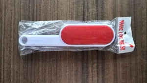 Double-sided magic lint brush with white handle and red fabric head for clothes dust cleaning.