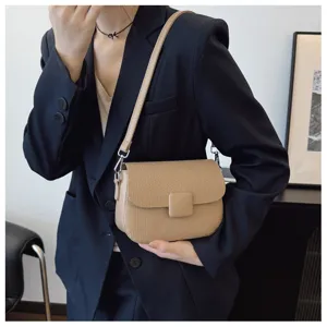 Side view of a vintage beige cross-body bag with textured flap and square clasp on model