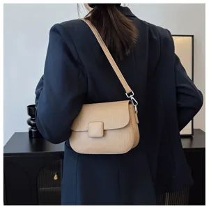 Minimalist beige textured leather crossbody bag with square clasp worn over a navy blazer