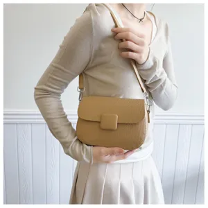 Close-up of a retro tan textured crossbody bag with square buckle detail.