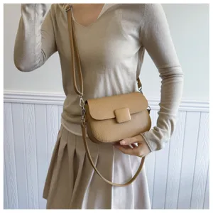 Detailed view of camel textured crossbody bag with square flap buckle worn by model.