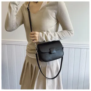 Close-up detail of a minimalist black textured flap crossbody bag worn by a model.