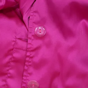 Close-up detail of hot pink satin shirt placket with transparent button and fine stitching.