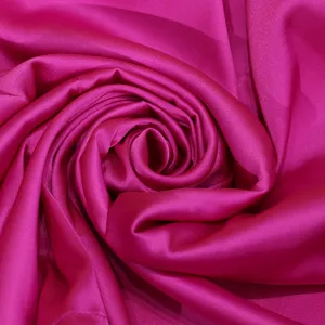 Detailed closeup of vibrant magenta satin fabric rolled in an elegant spiral shape.