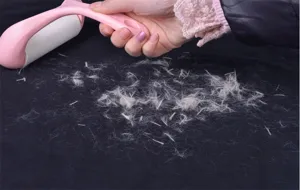 Detailed close-up shot of a pink lint roller cleaning pet hair and dust from dark fabric.
