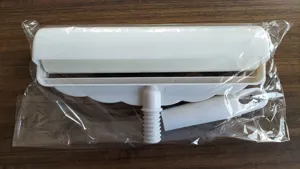 Detailed view of white lint roller with sticky paper and handle connector in transparent package.