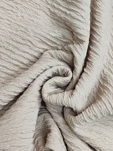 Close-up detail shot of light khaki textured pleated fabric showing intricate weave and crinkled design.
