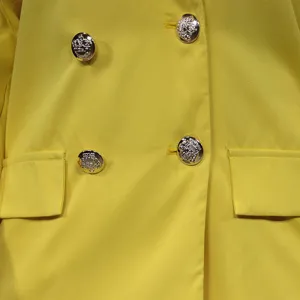Nahaufnahme eines gelben Zweireiher-Blazers mit silbernen geprägten Knöpfen und Taschen.