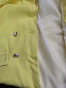 Nahaufnahme der gelben Damenblazer-Details mit Metallknöpfen und weißem Futter handwerklich.