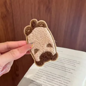 Close-up view of a cute fuzzy cartoon cat hair patch held against a book background.