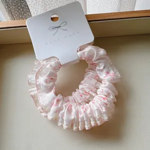Detail view of a white cotton scrunchie with pink polka dots and bow pattern lace edge