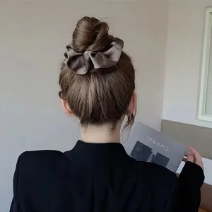 Detail of a coffee brown satin scrunchie styled on a classic bun hair style.