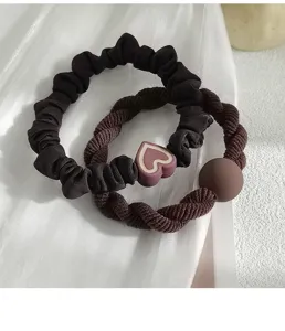 Detailed view showing a dark brown ruffled scrunchie and heart charm elastic hair tie