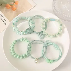 Detailed view of six mint green elastic hair ties with various decorative pearls and bows