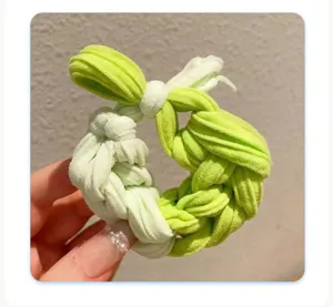 Close-up of a braided green fabric hair tie held by hand against a wall
