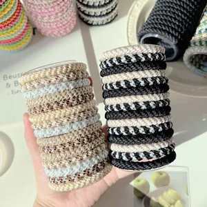 Detailed view of beige and black braided high-elasticity hair ties held in hand