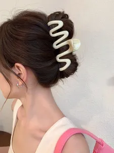 Detailed shot of a wavy cream white hair claw clip holding a stylish bun on a woman's hair.