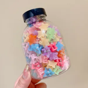 Detail view of various colorful star-shaped mini hair claw clips in a clear storage jar