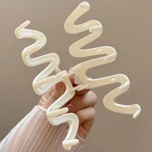Close-up macro shot of a minimalist cream white wave-shaped hair claw clip held in hand