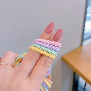 Close-up detail of colorful ruffled macaron hair elastics held on fingers for little girls.